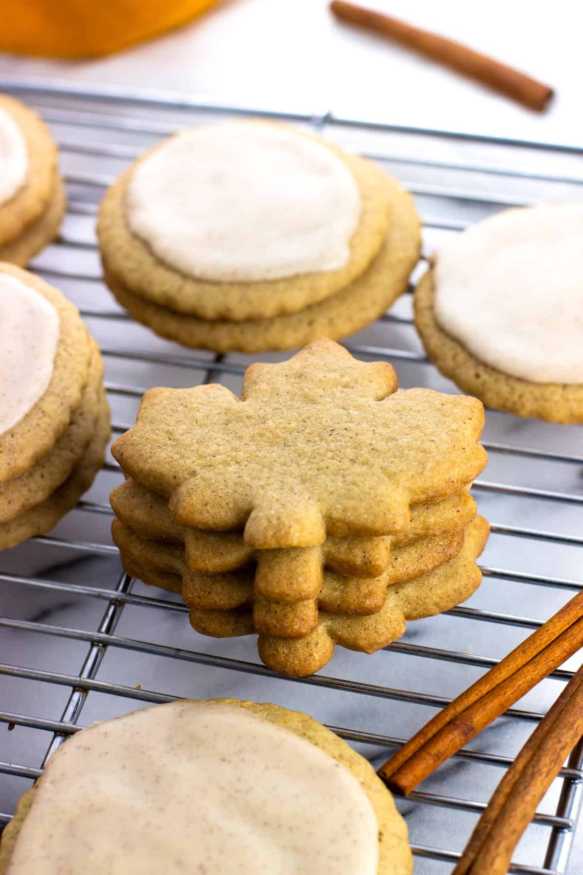 A stack of un-iced maple leaf shaped cookies on a rack.