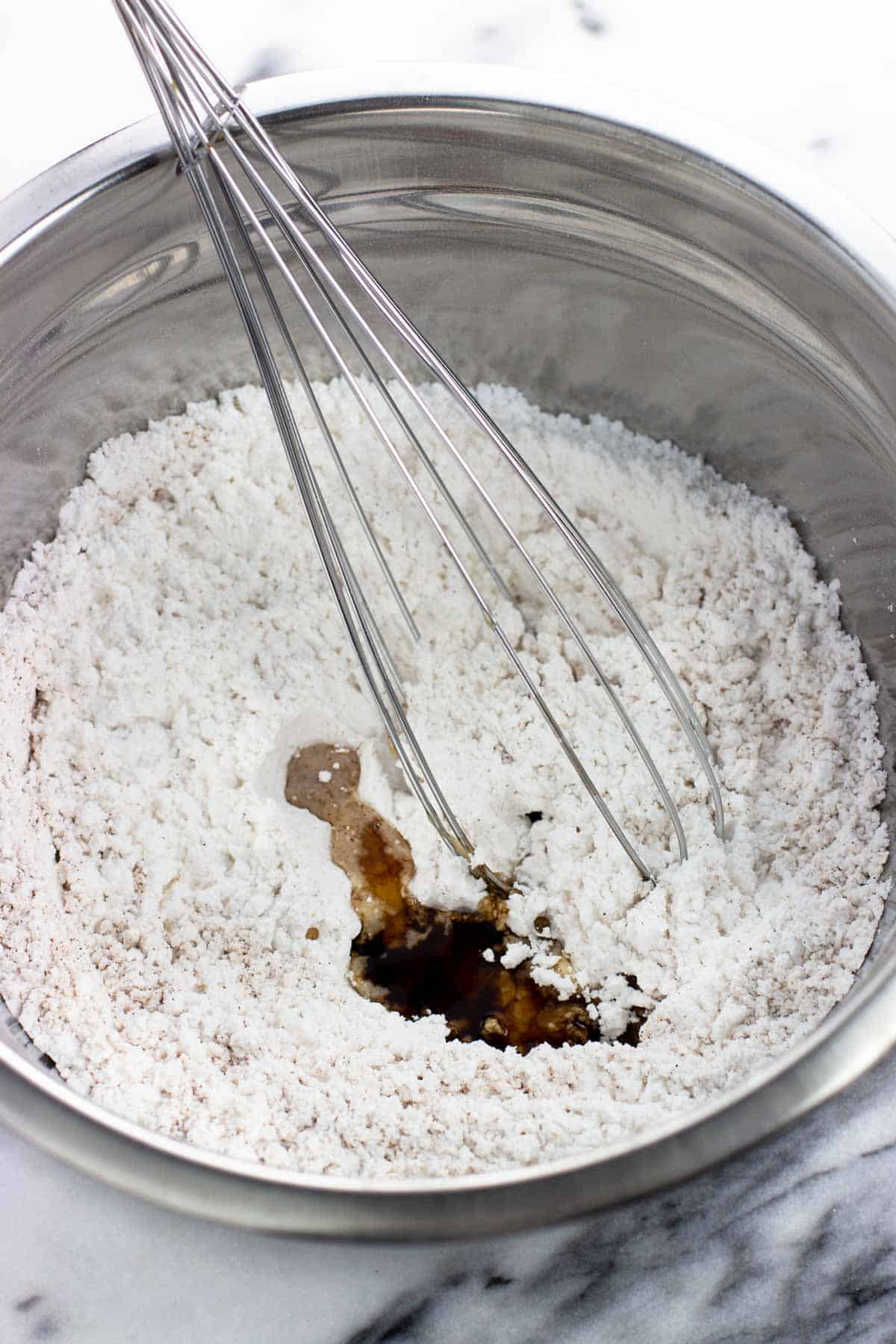 Powdered sugar, cinnamon, and extracts added to a bowl with a whisk.