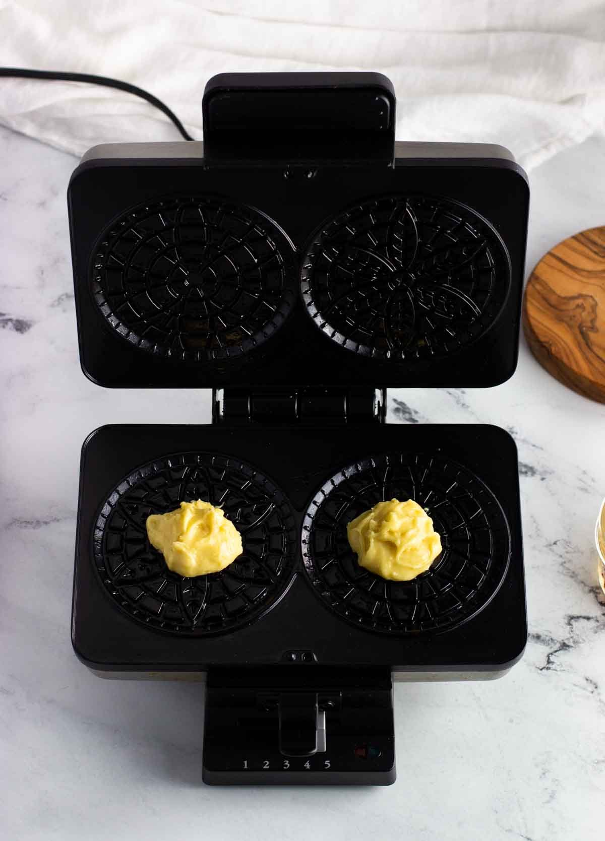 Two ball of batter on the open pizzelle press.