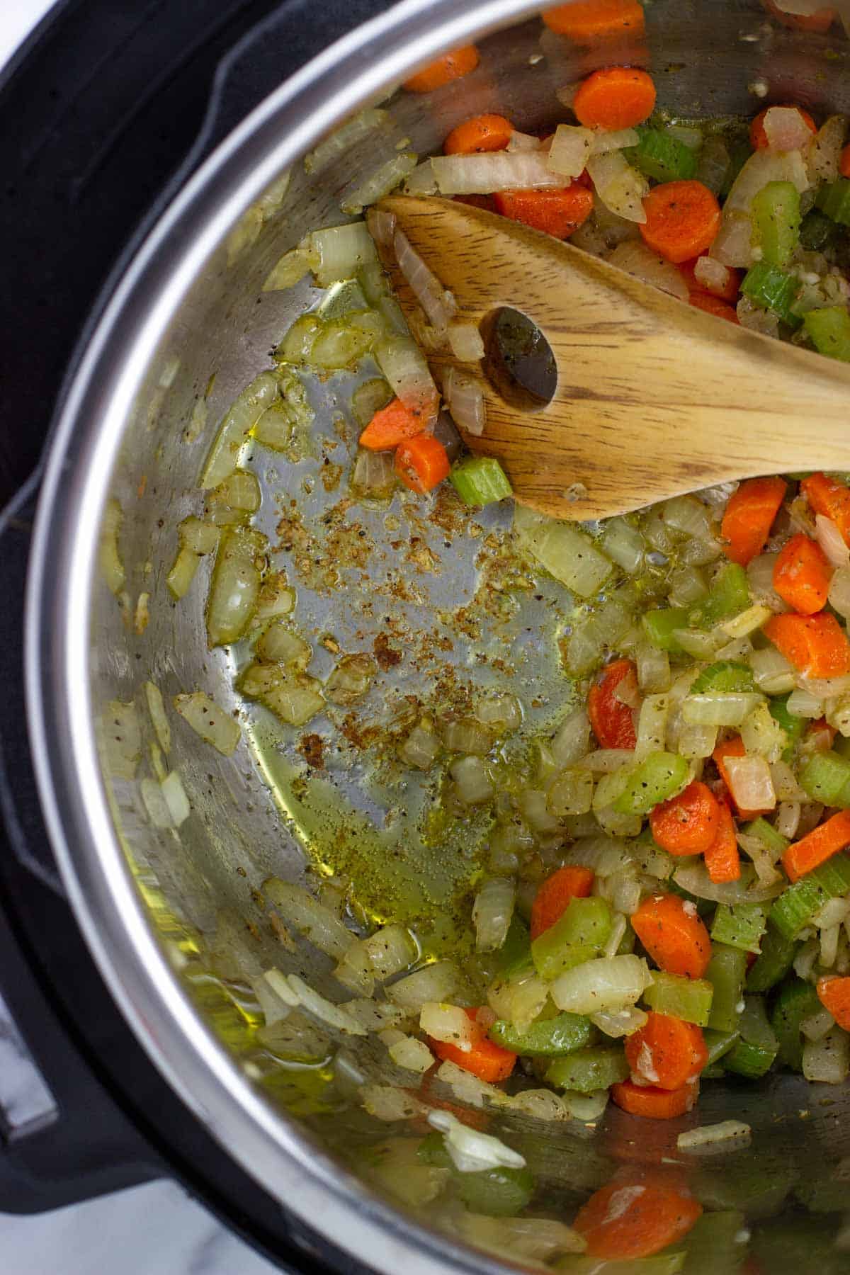 A wooden spoon scraping up fond from the bottom of the Instant Pot.