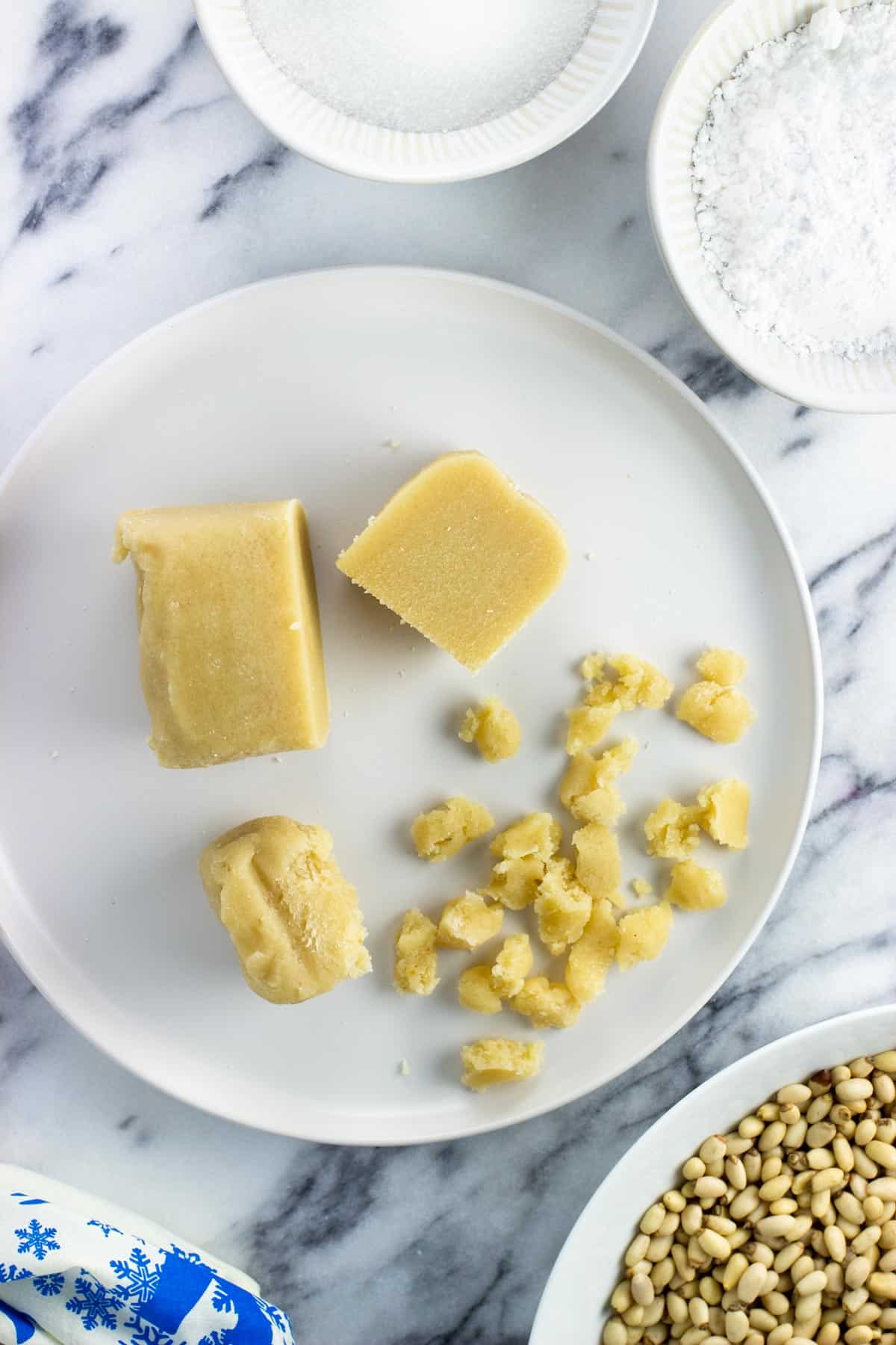 A block of almond paste on a plate cut in half with some of it crumbled.