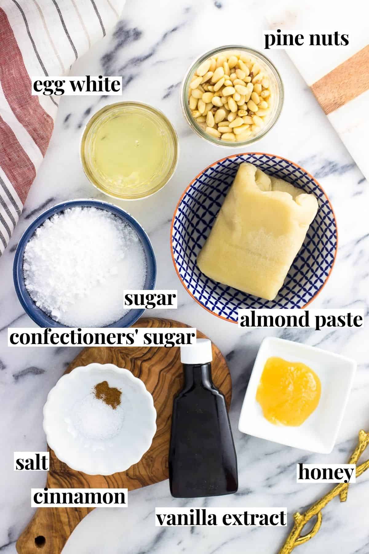 Labeled pignoli cookie ingredients on a marble board.