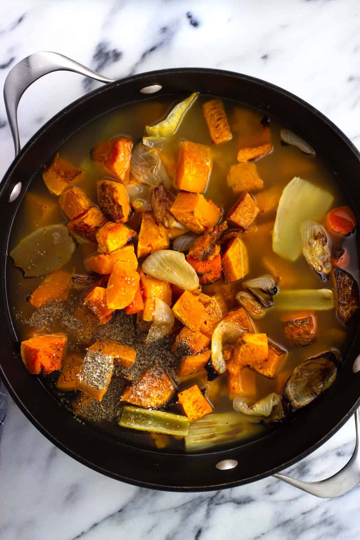 Roasted squash and other vegetables in a large pot with broth and spices.
