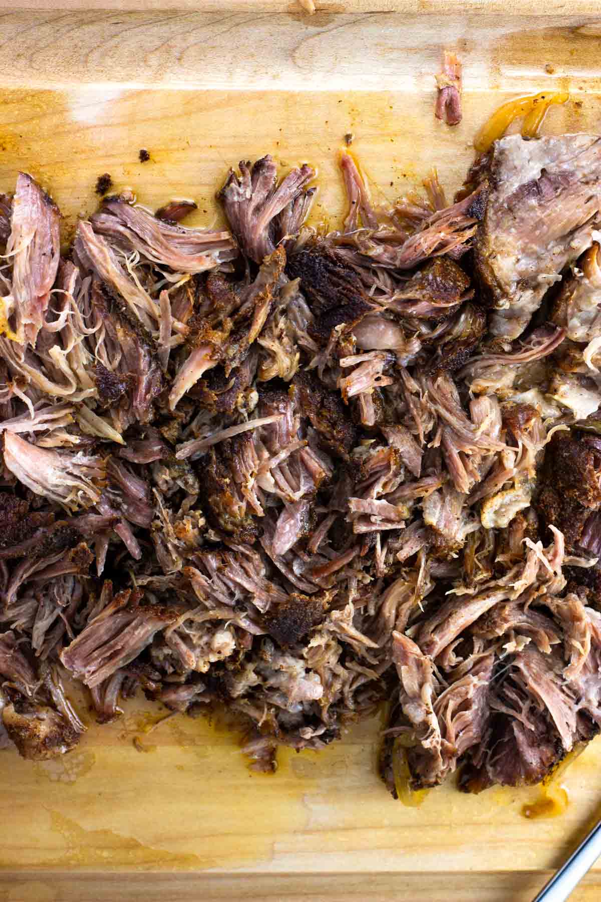 Shredded pulled pork on a wooden cutting board.