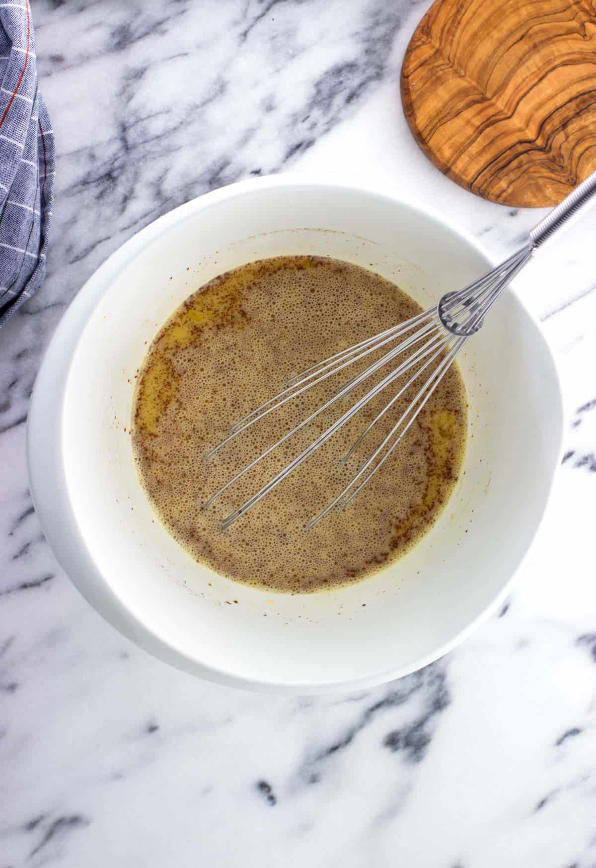 Eggs, milk, maple syrup, and cinnamon whisked together in a bowl.