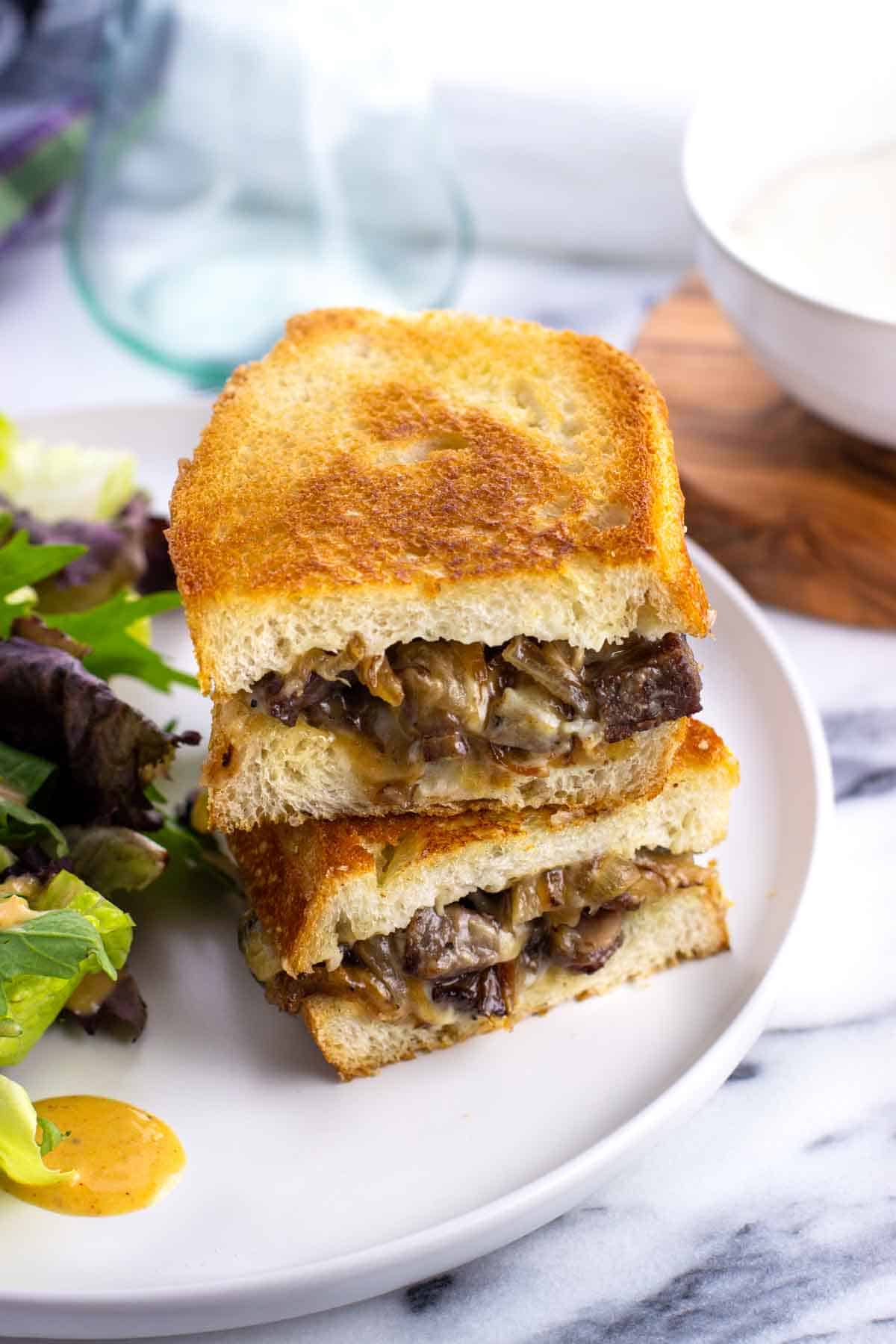 A steak sandwich and side salad on a plate.