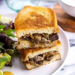 A steak sandwich on a plate with a salad.