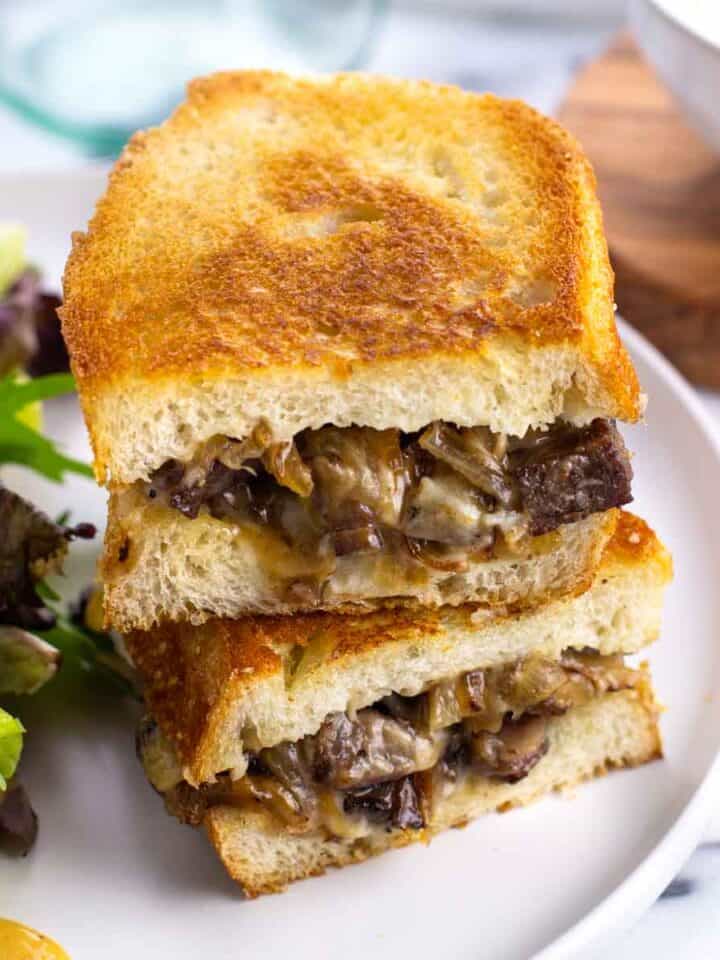 A steak sandwich on a plate with a salad.