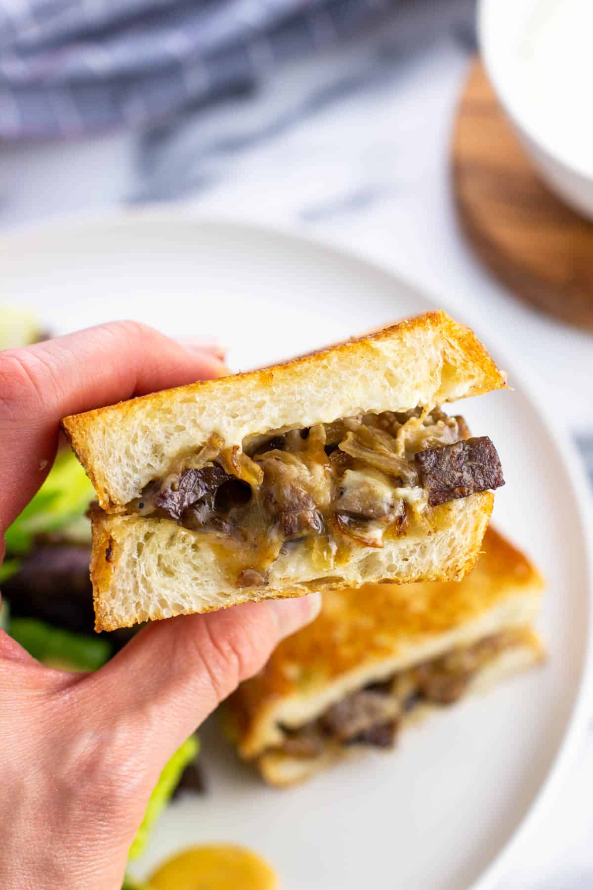 A hand holding up half of a leftover steak sandwich.