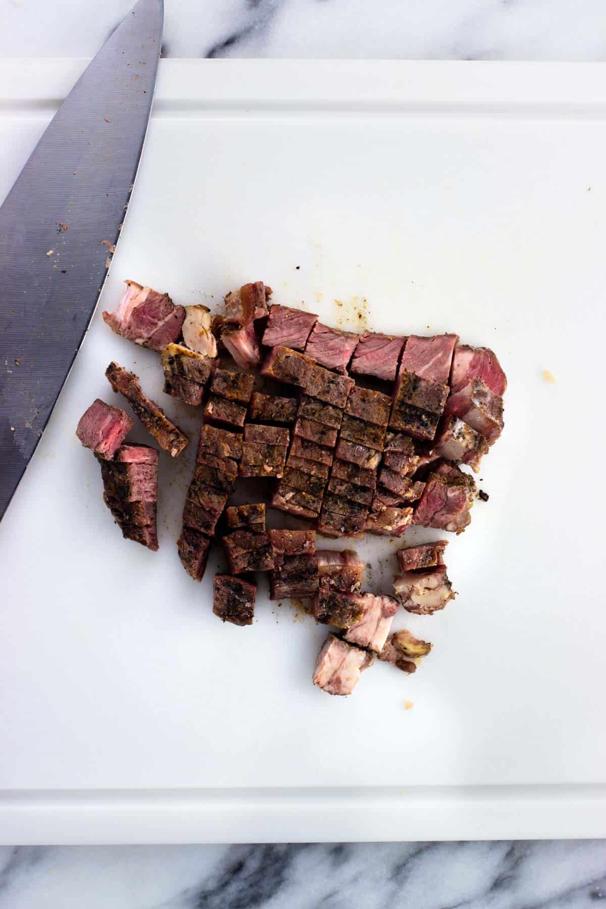 Chopped up leftover cooked steak on a cutting board.