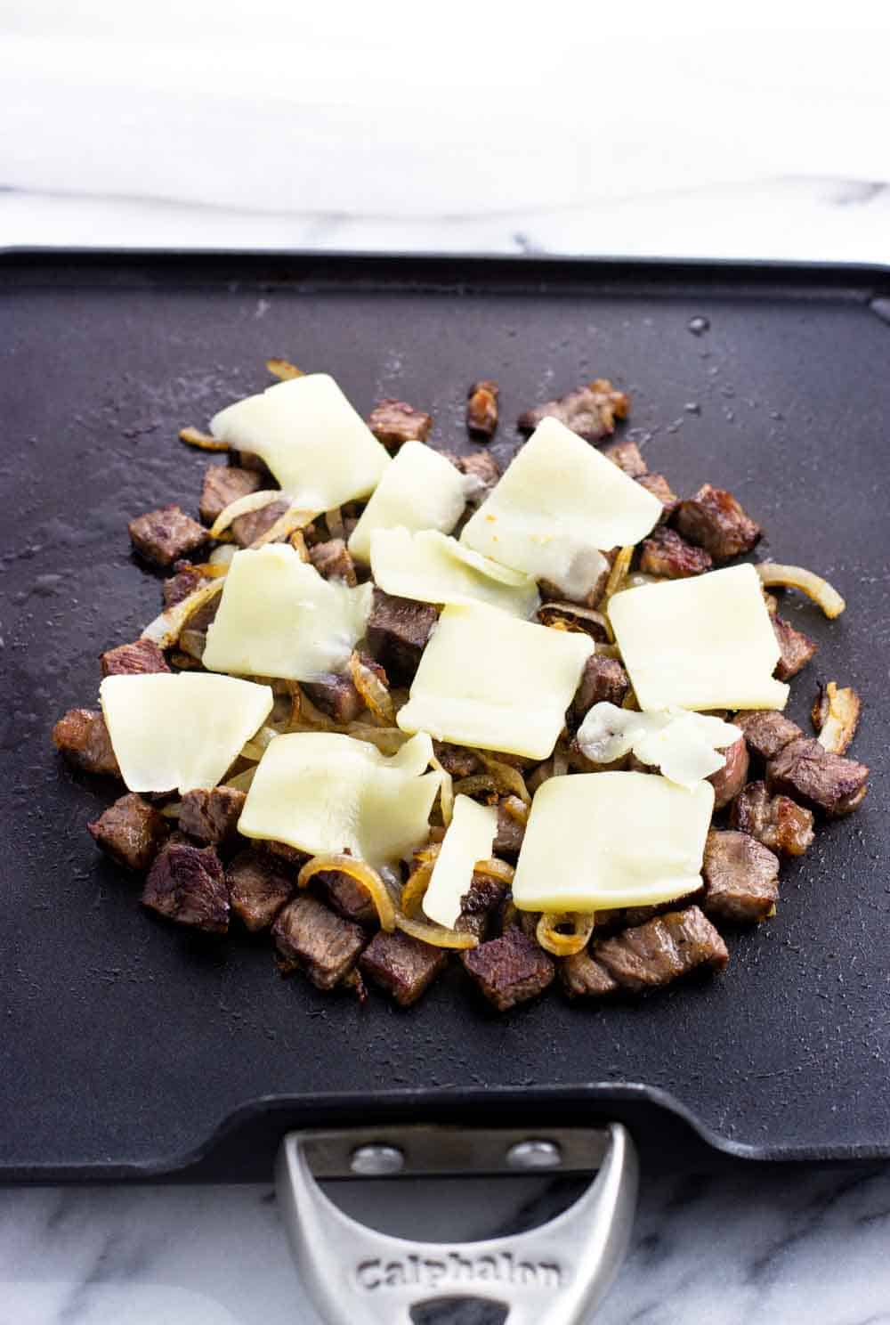 Pieces of cheese on top of the steak and onion on the pan.