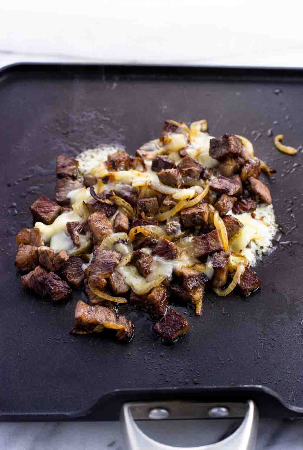 Melted cheese mixed into the steak and onion on a pan.