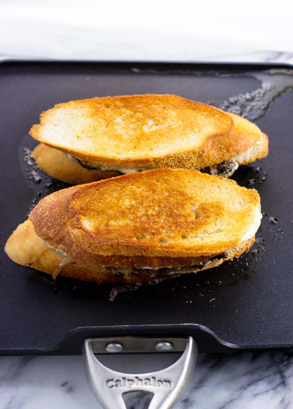 Two steak sandwiches on a griddle pan.