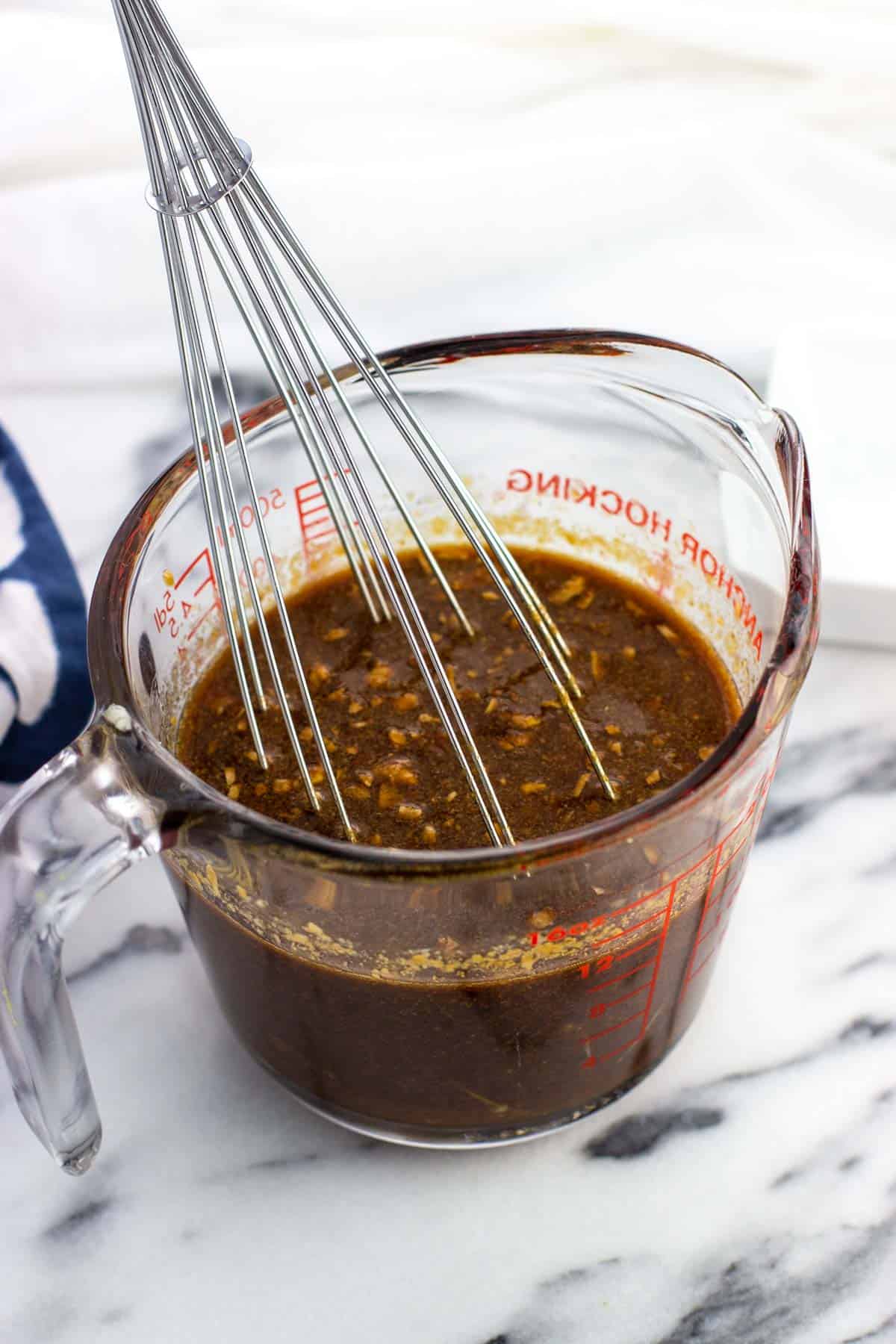 A whisk in a glass measuring cup with the stir fry sauce.