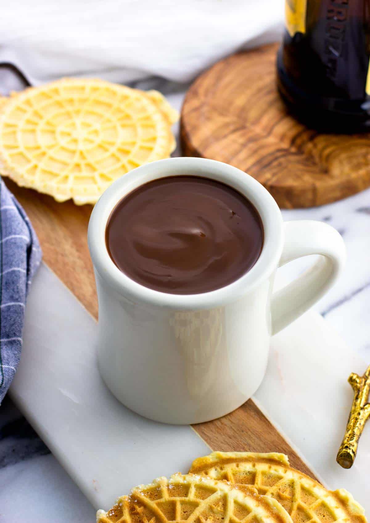 A ceramic mug filled with Italian hot chocolate surrounded by pizzelle.