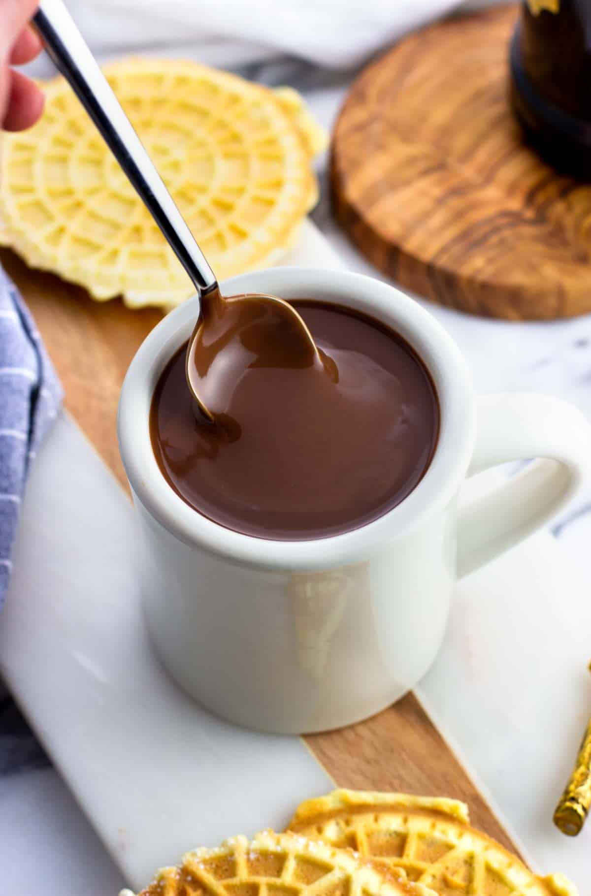 A spoon being dunked into a mug of thick hot chocolate.