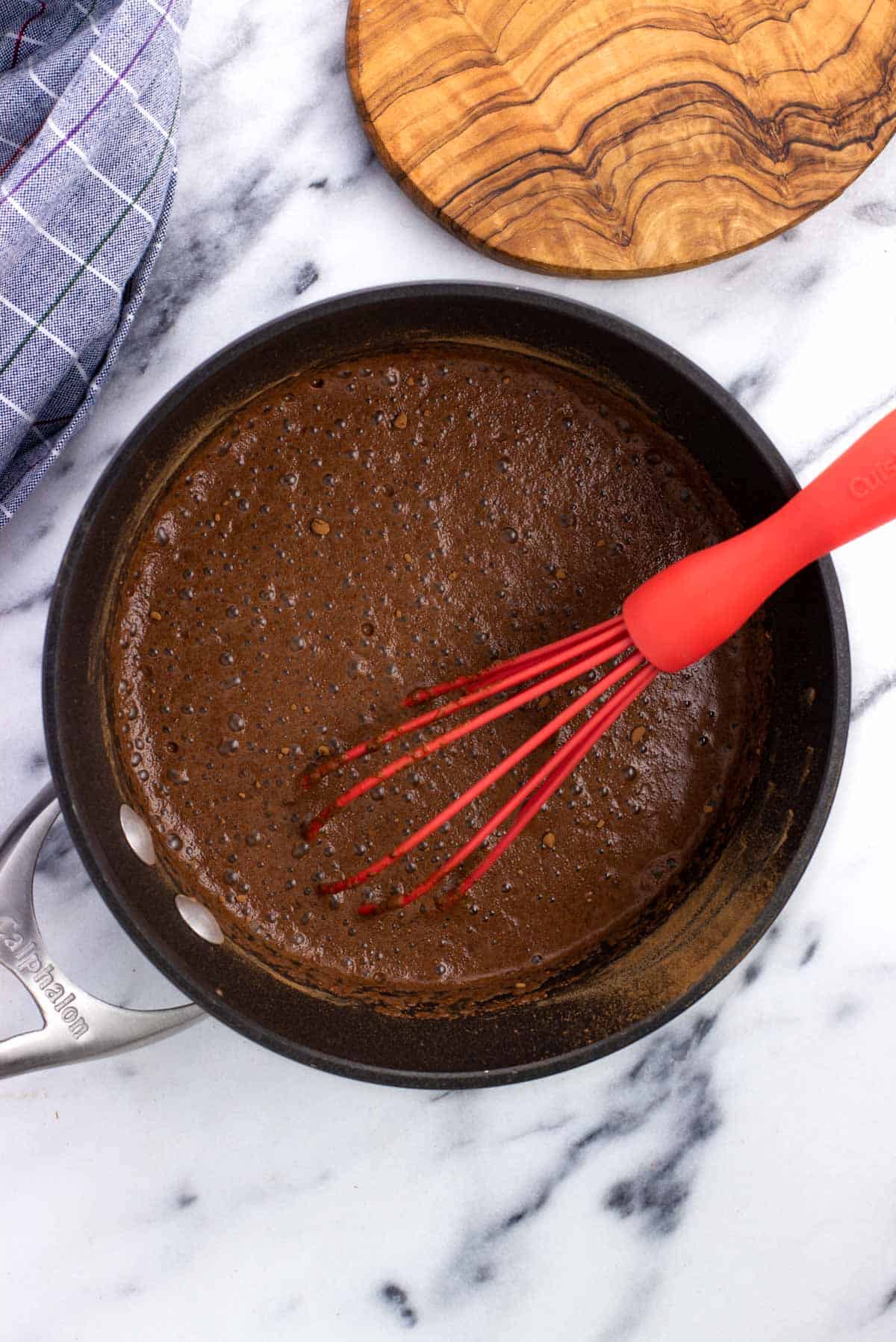 Milk poured into the pan with the dry ingredients with a whisk in it.