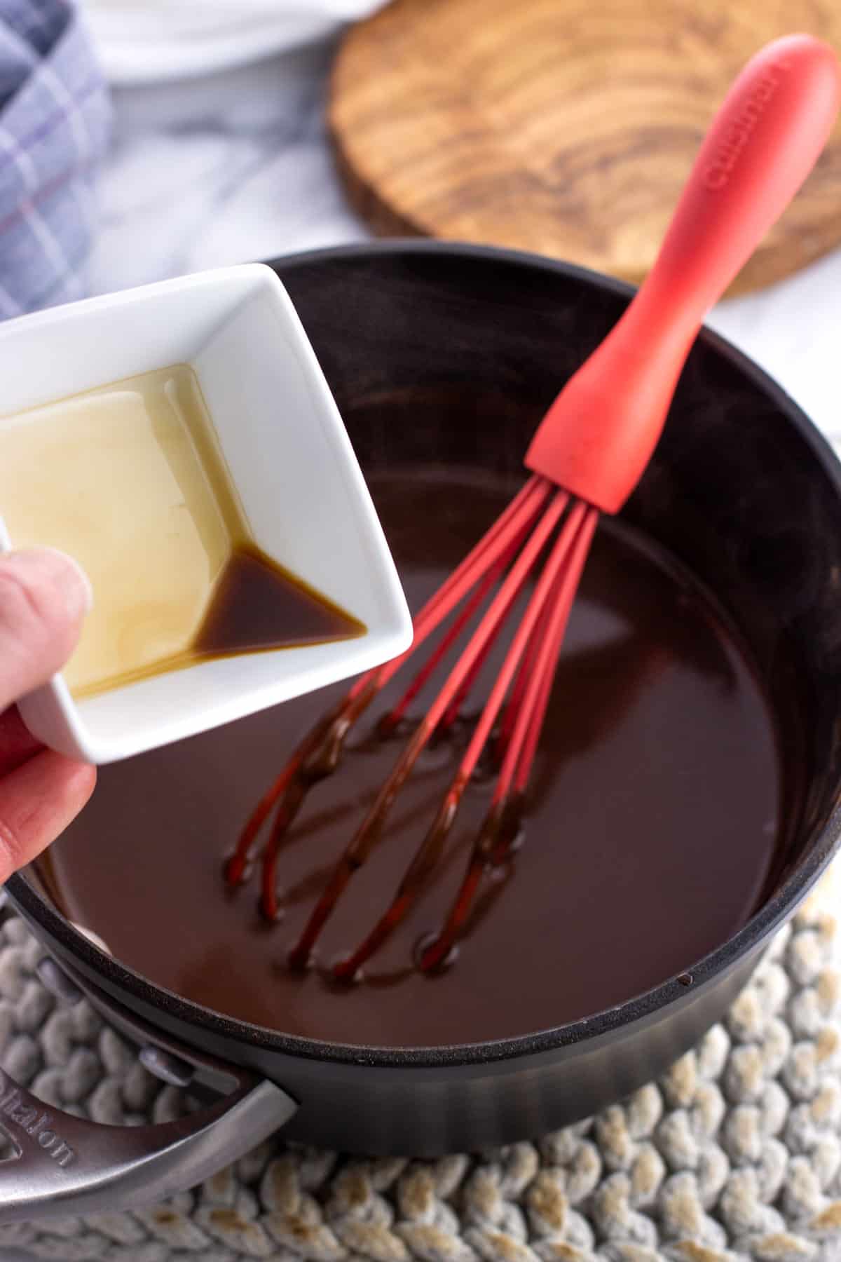 Vanilla extract being poured into the pan of hot chocolate.