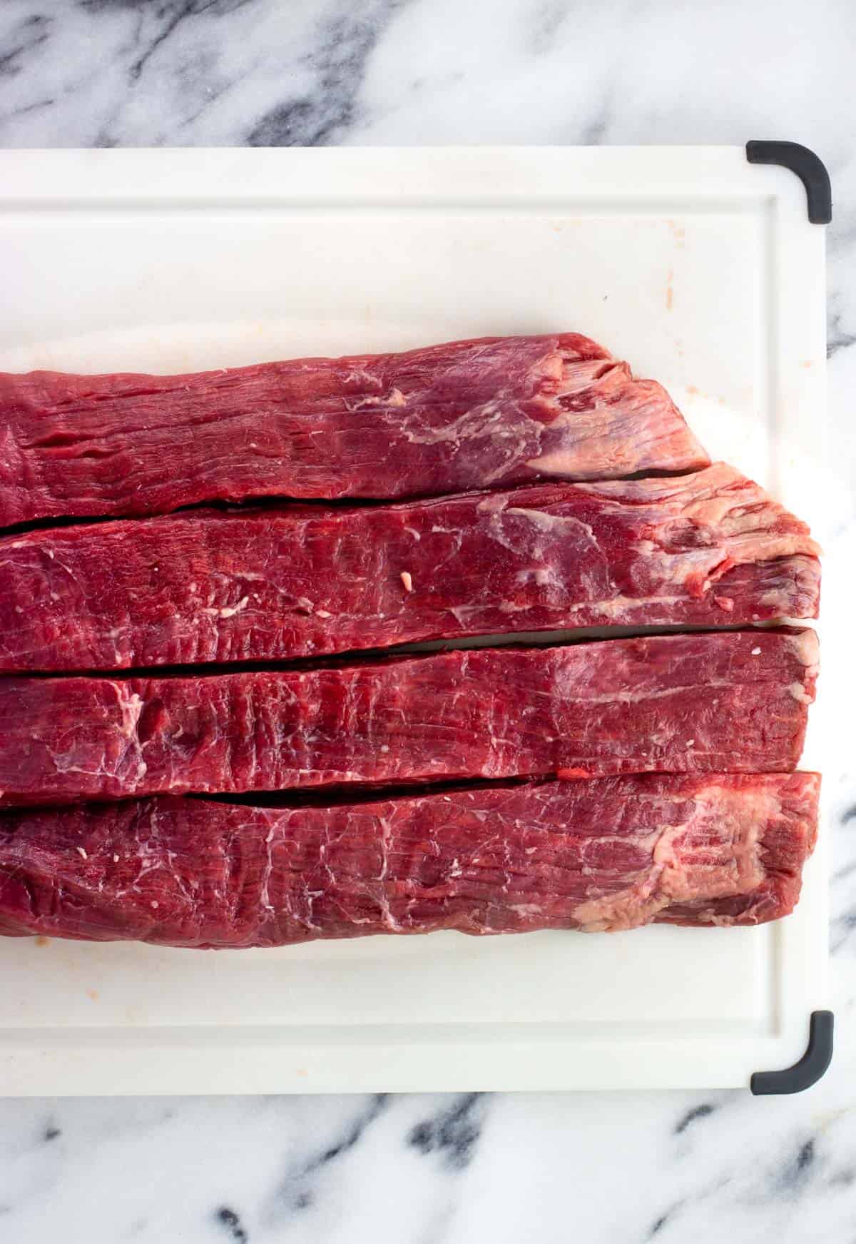 Flank steak on a cutting board cut into horizontal strips.