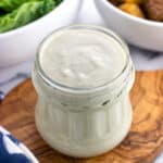 A glass jar of caesar dressing with salad ingredients in the background.