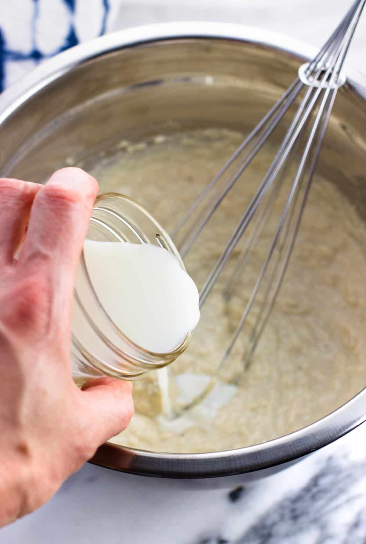 Milk being poured into the bowl with the dressing ingredients.