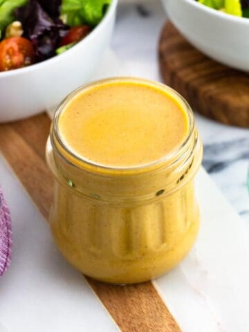 A jar of hummus salad dressing surrounded by bowls of salad.