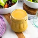 A jar of hummus salad dressing surrounded by bowls of salad.