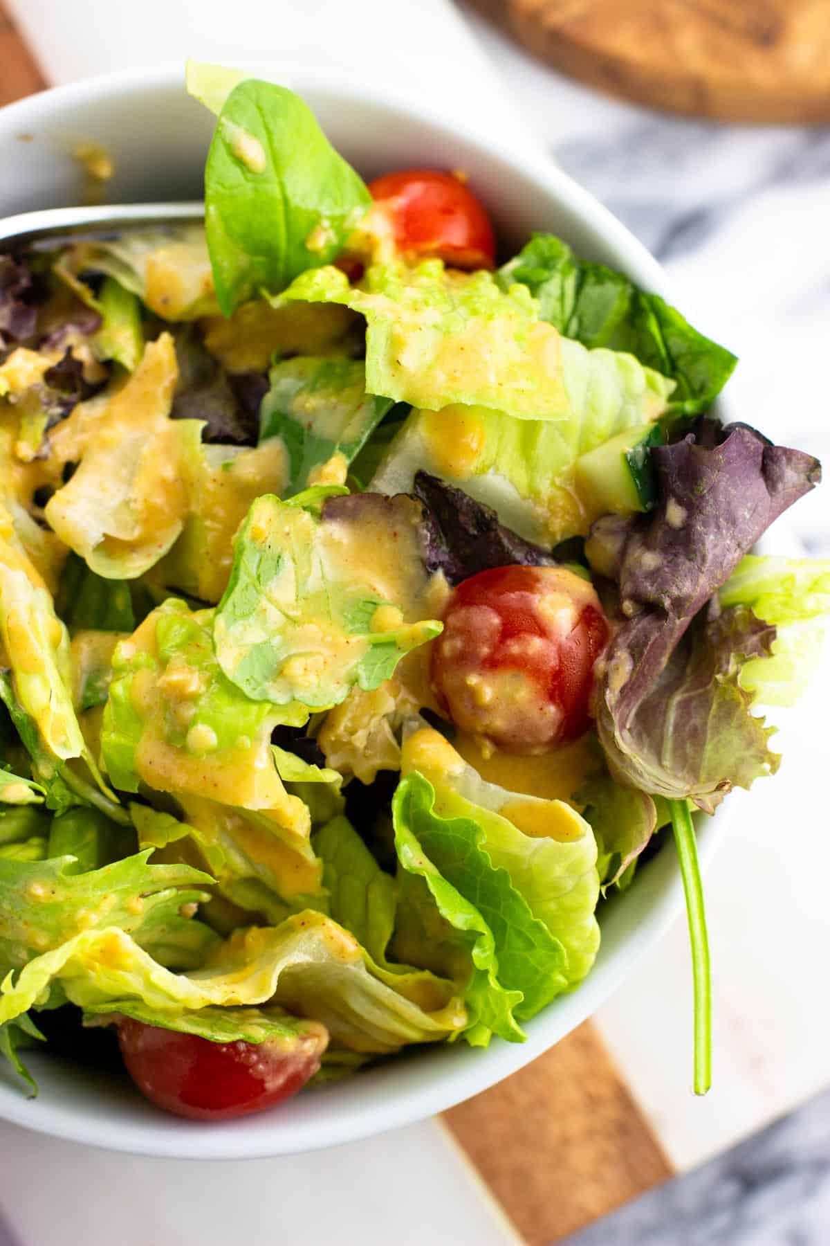 A dressed mixed green salad with hummus dressing and tomatoes in a bowl.