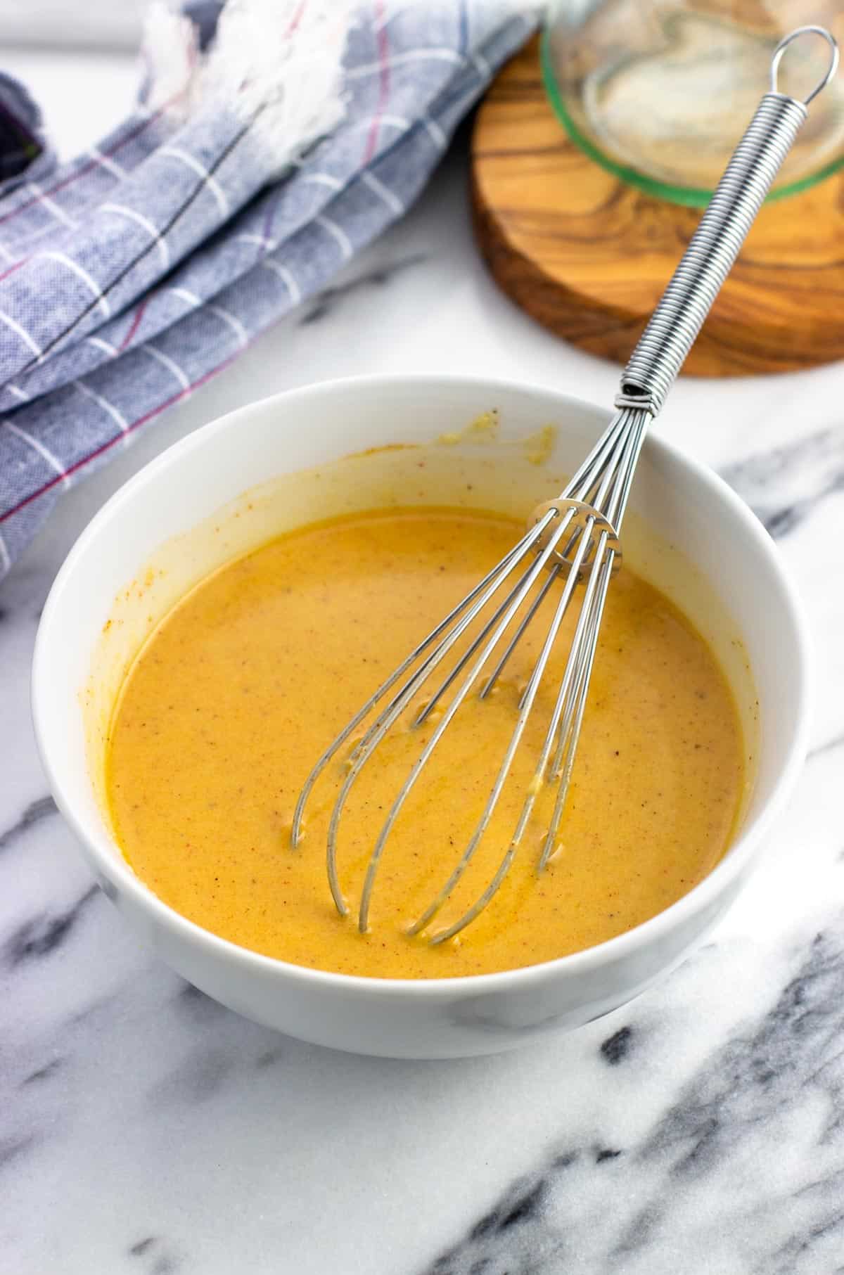 Combined hummus dressing with a whisk in a bowl.