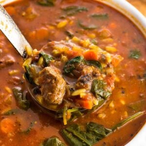 A ladle lifting a heaping serving of vegetable beef soup out of a pot.