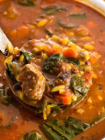 A ladle lifting a heaping serving of vegetable beef soup out of a pot.