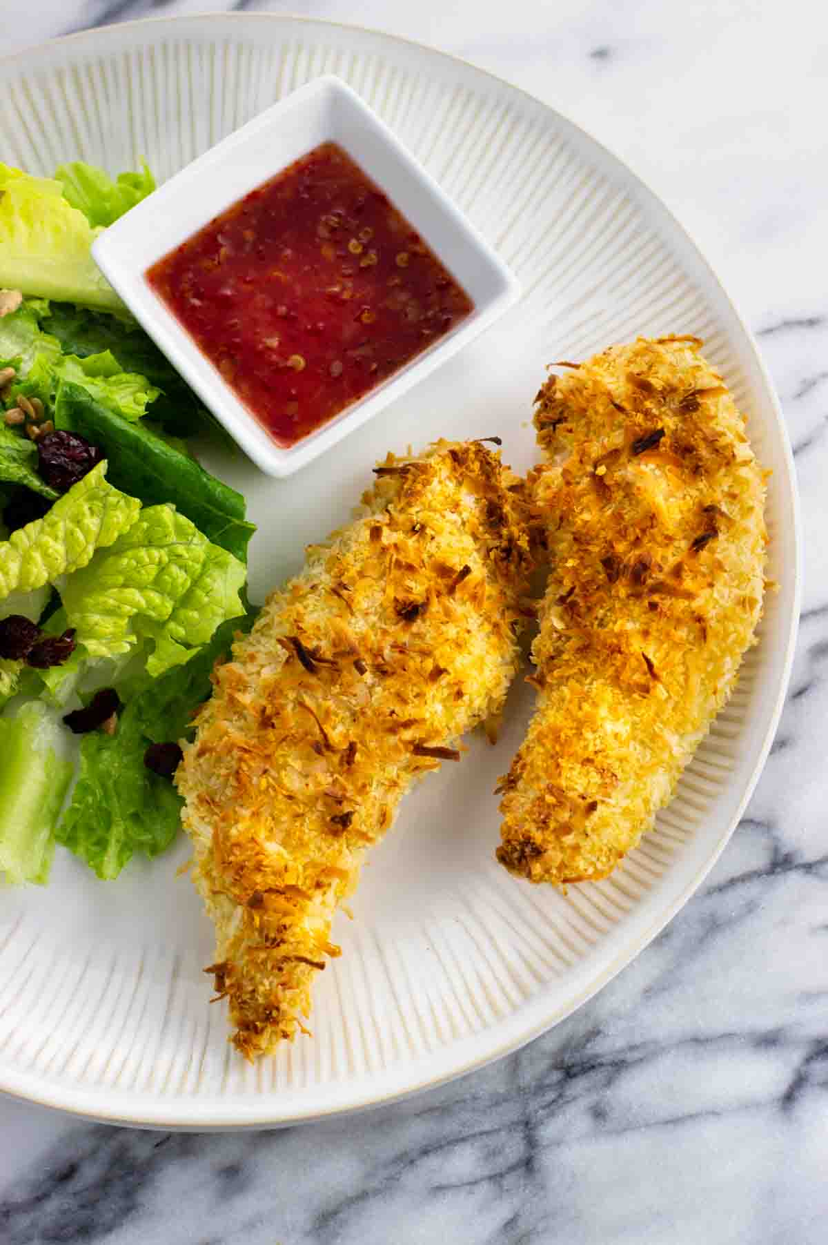 Two chicken tenders on a plate with salad and dipping sauce.