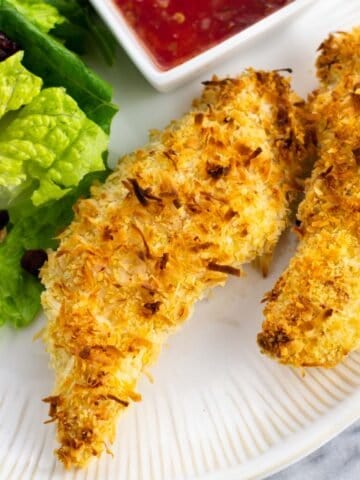 Two chicken tenders on a plate with salad.