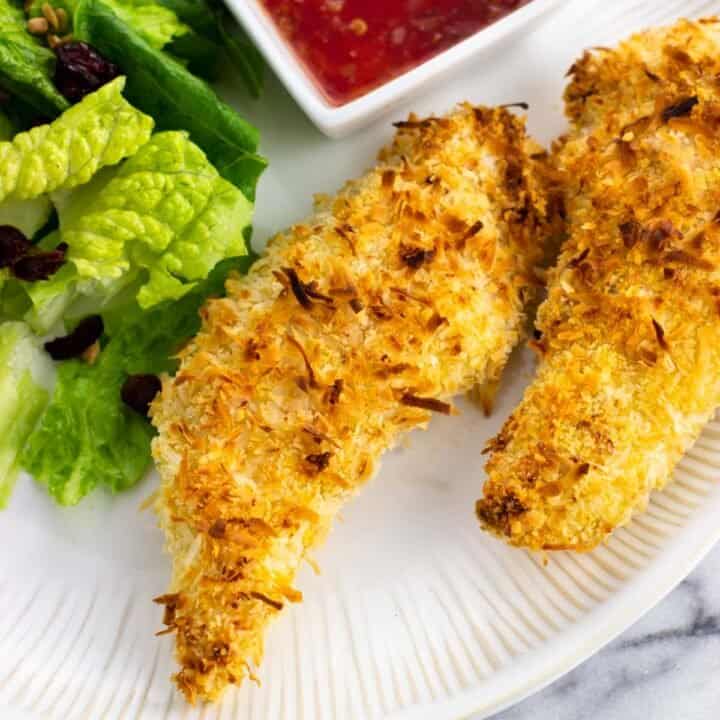 Two chicken tenders on a plate with salad.