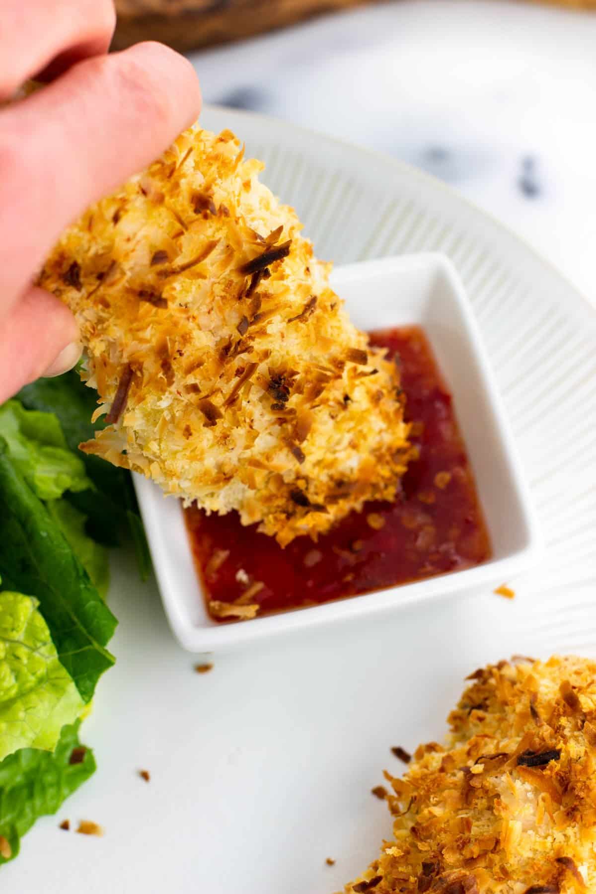 A chicken tender being dipped in a small ramekin of sweet chili sauce.