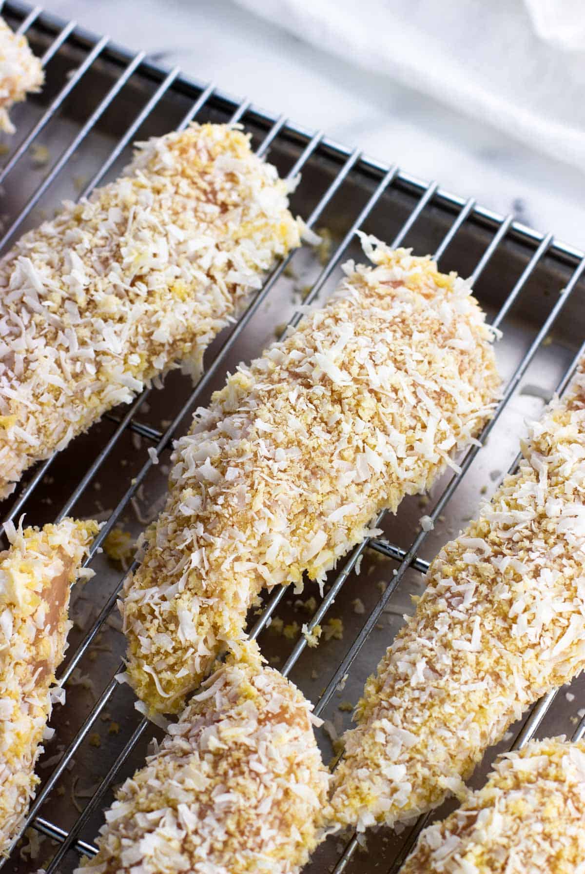 Raw panko and coconut coated tenders on a rack.