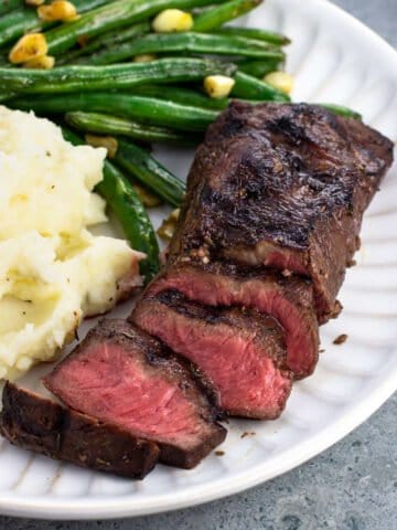 Half-sliced steak on a plate with mashed potatoes and green beans.