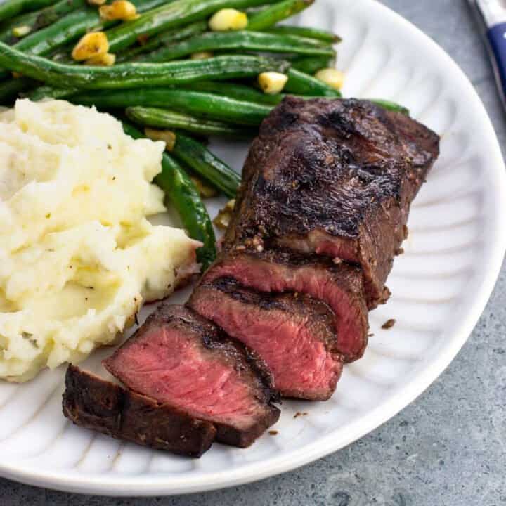 Half-sliced steak on a plate with mashed potatoes and green beans.