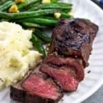 A sliced steak with mashed potatoes and green beans.