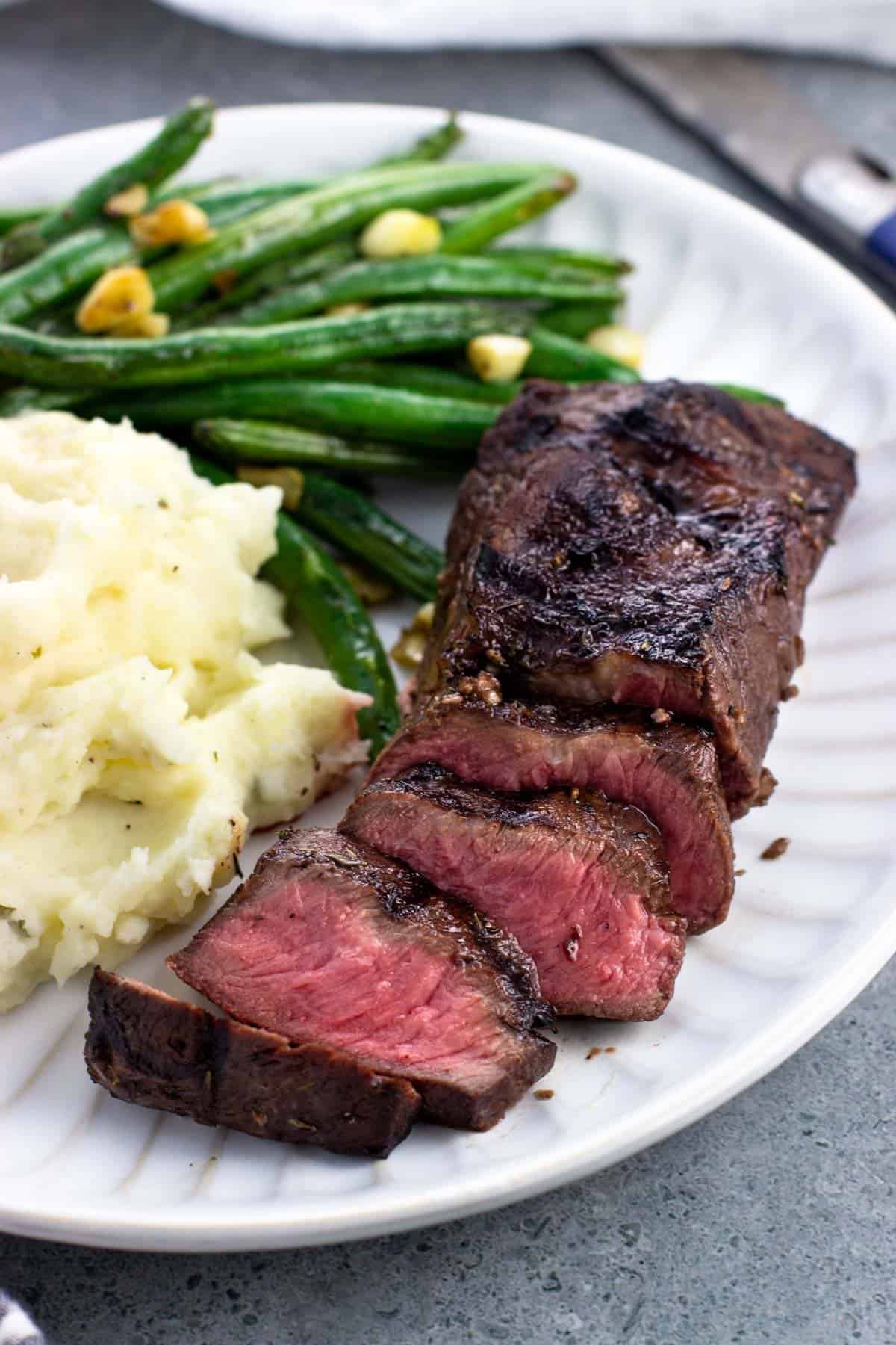 A sliced steak with mashed potatoes and green beans.