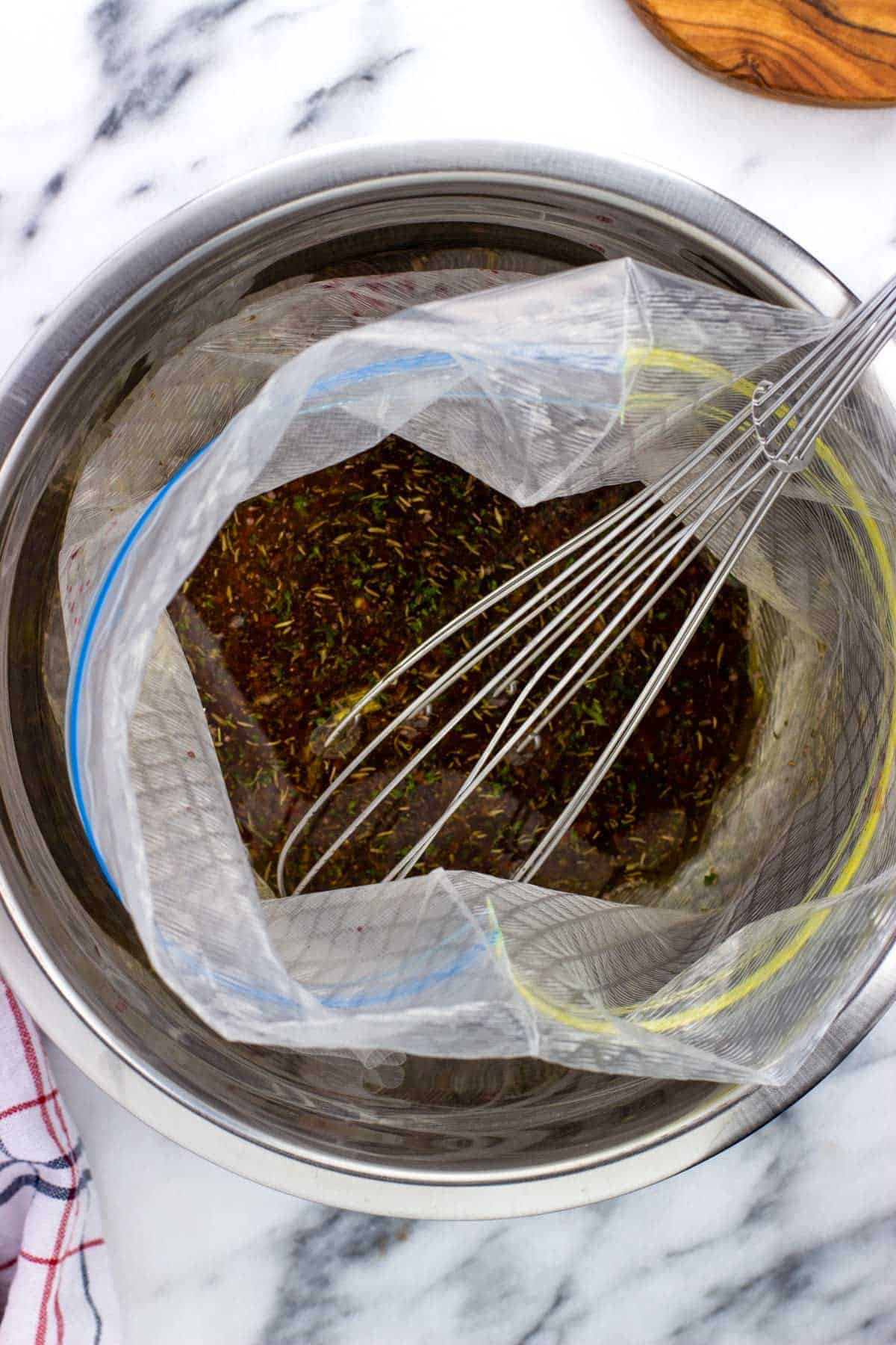 A whisk in a large plastic bag filled with the flat iron steak marinade.