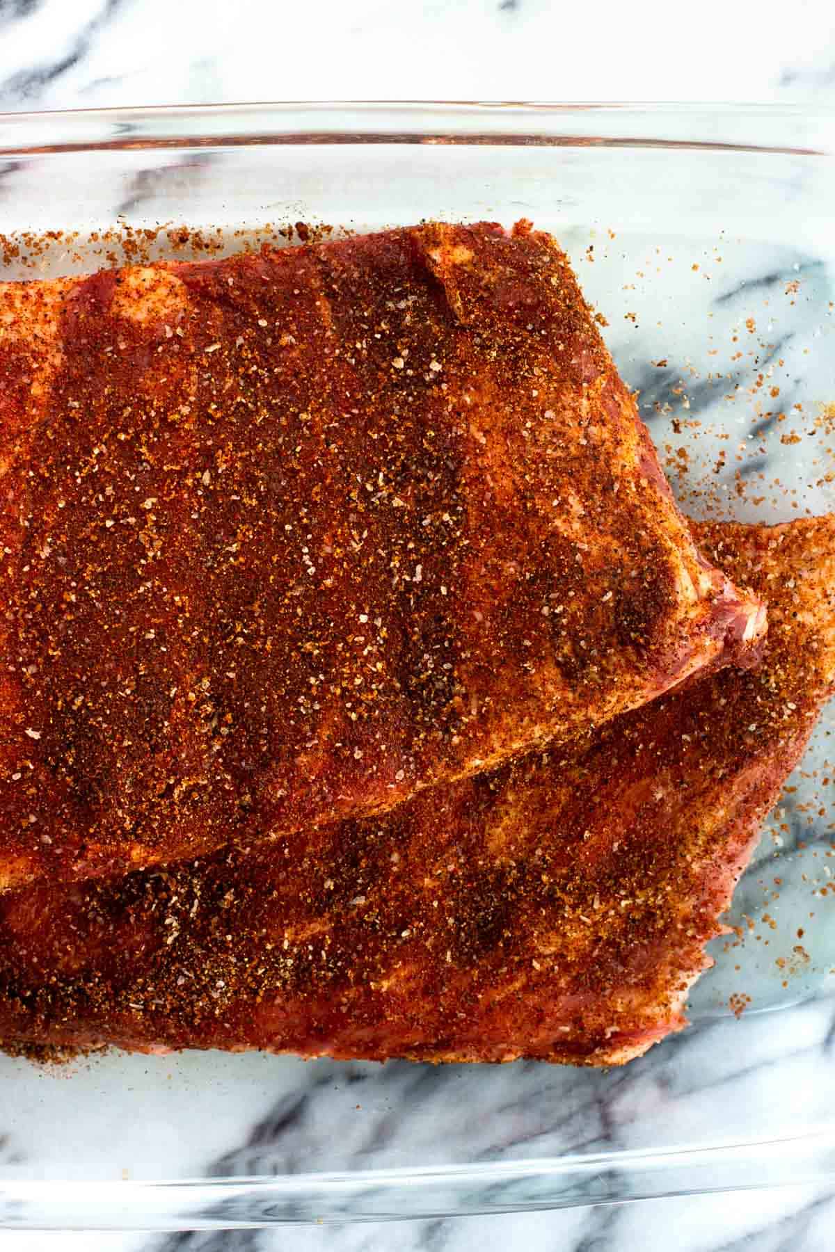 Spice rubbed raw ribs in a glass dish.