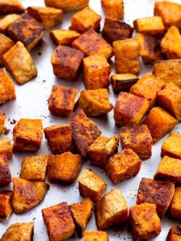 Well-roasted sweet potato cubes on a sheet pan.