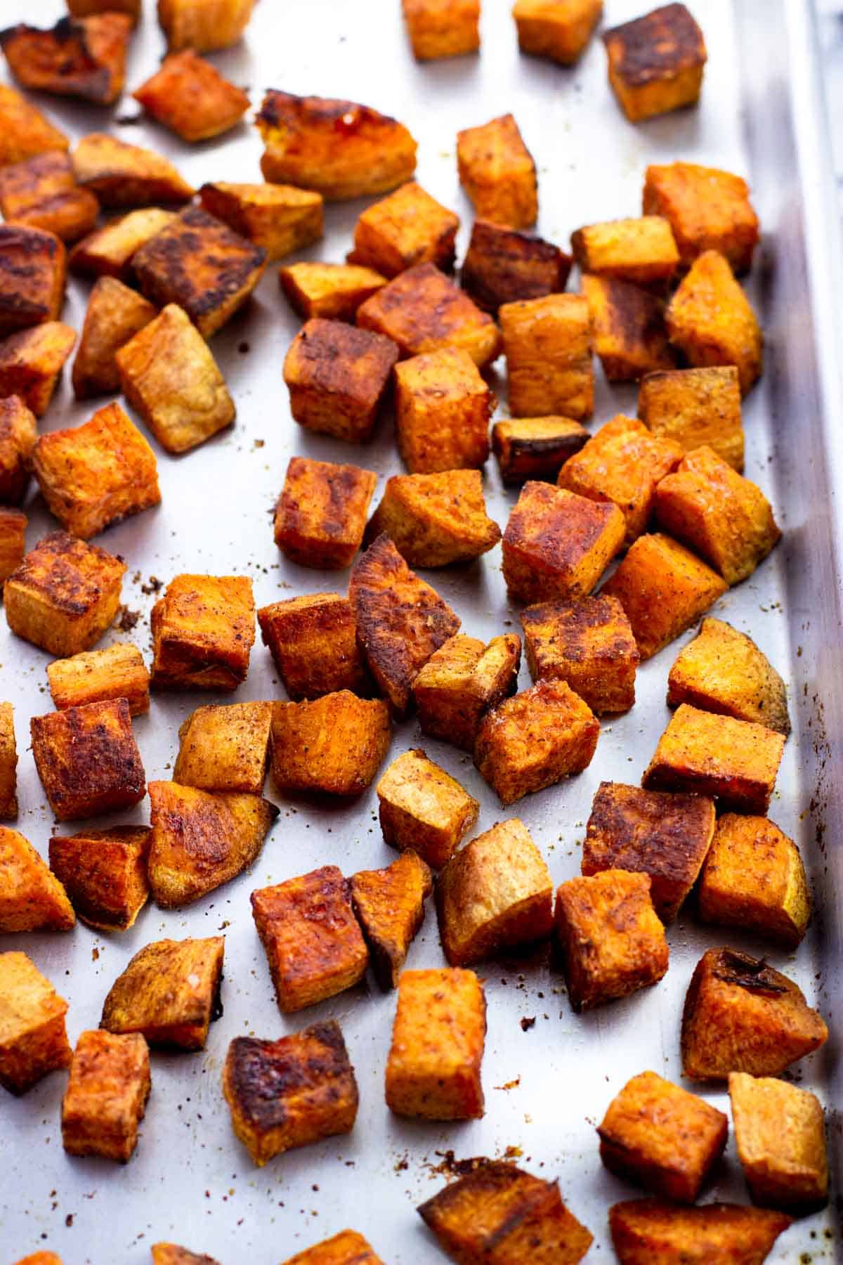 Roasted sweet potato cubes on a metal sheet pan.
