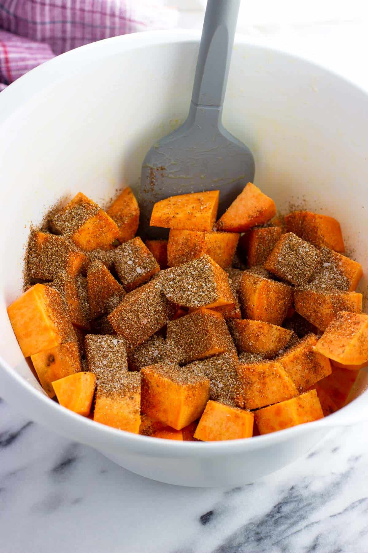 Sweet potato cubes in a mixing bowl topped with dry seasoning.