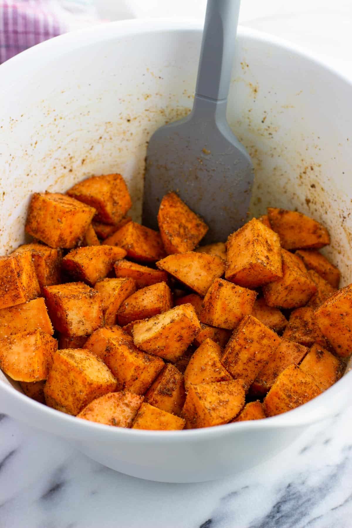 Seasoned cubes of sweet potato in a bowl with a spatula.