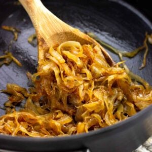 A wooden spoon scooping caramelized onions in a saucepan.