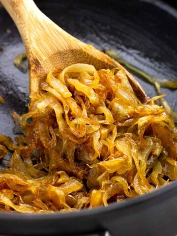 A wooden spoon scooping caramelized onions in a saucepan.