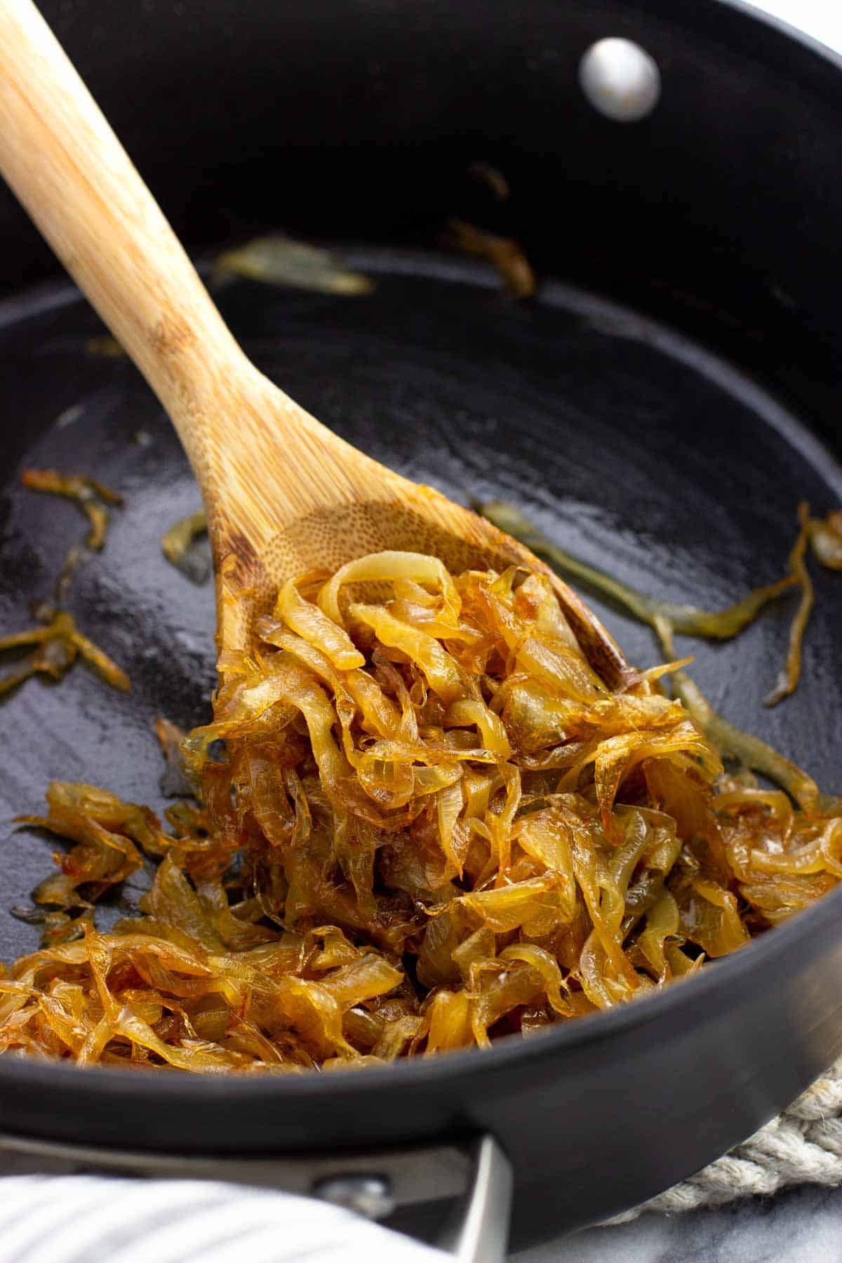 A wooden spoon scooping caramelized onions in a saucepan.