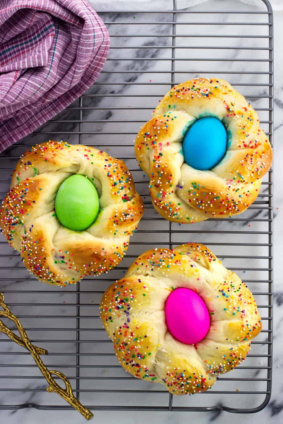 Three Italian Easter bread loaves on a wire rack.